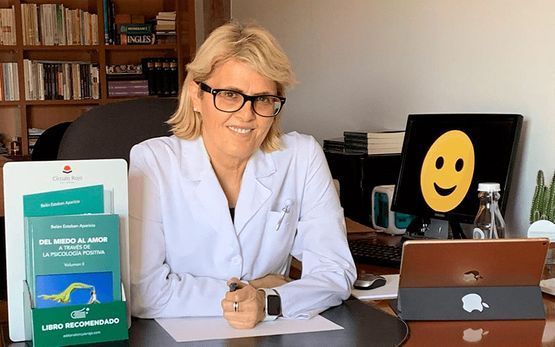 Una mujer con una bata blanca está sentada en un escritorio con una computadora portátil.